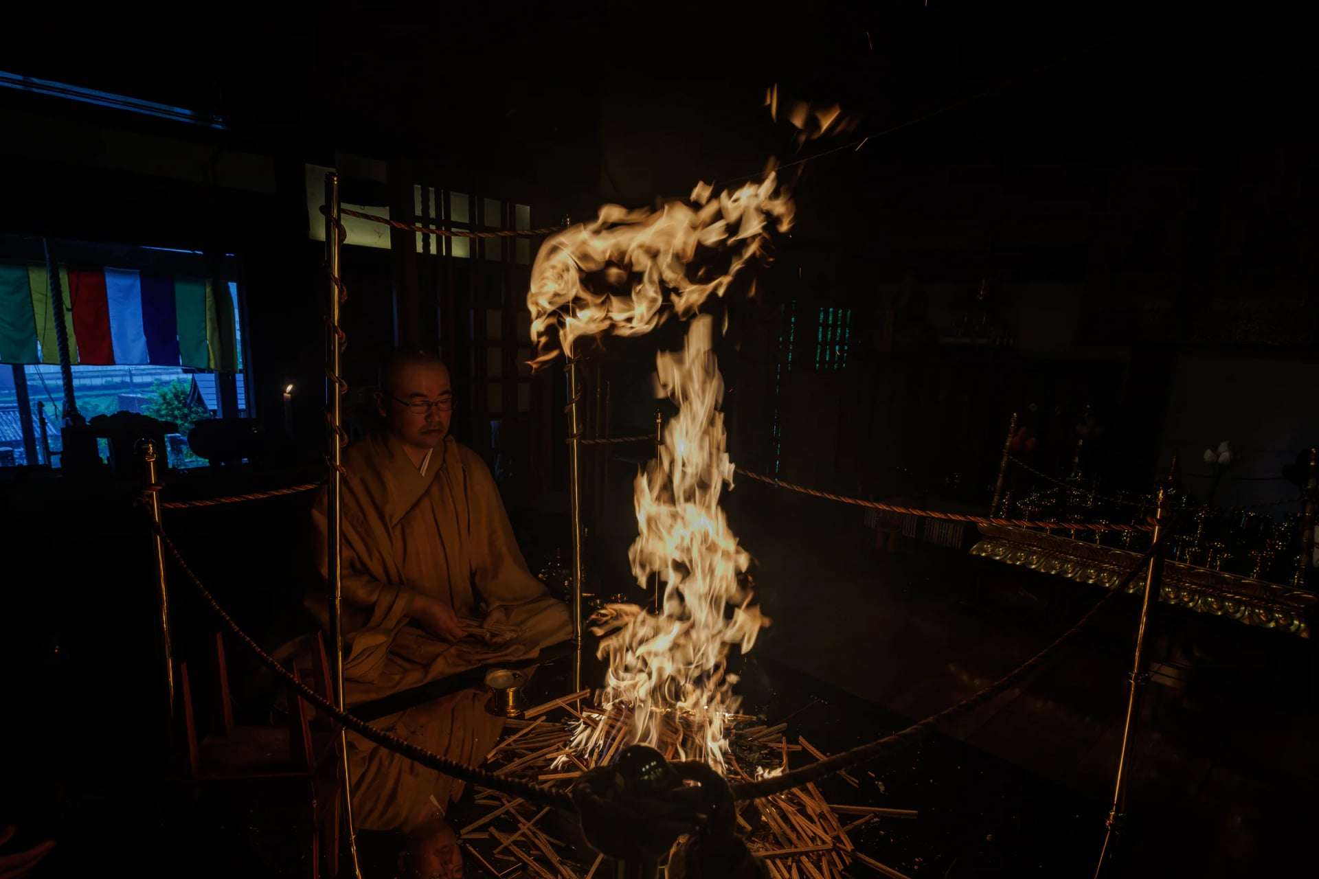 The wisdom-fire rising from the goma altar in the dark hall